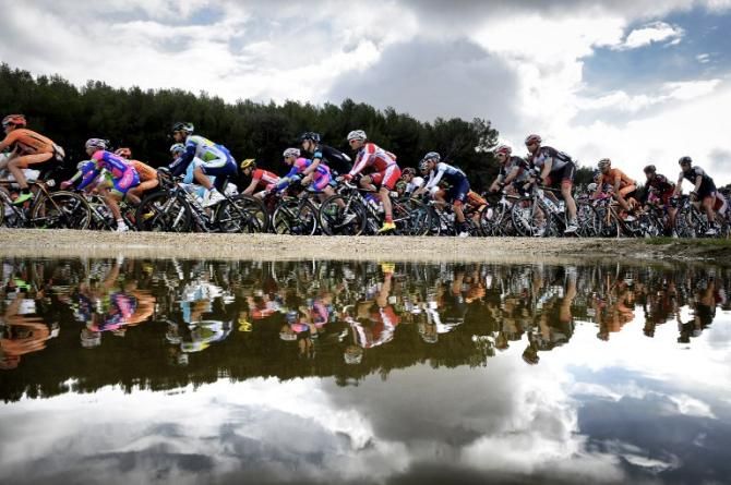 Riders reflected on a passing pond in Paris-Nice