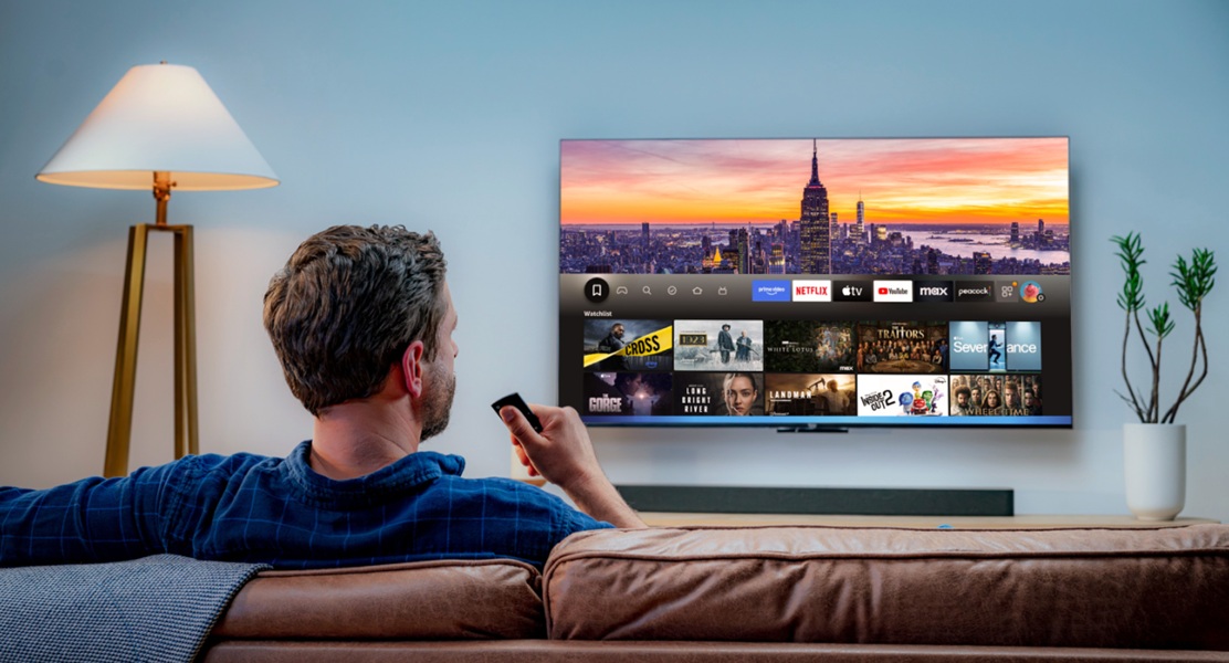 A model watching their Amazon Fire TV with the remote close by, speaking to Alexa Plus.