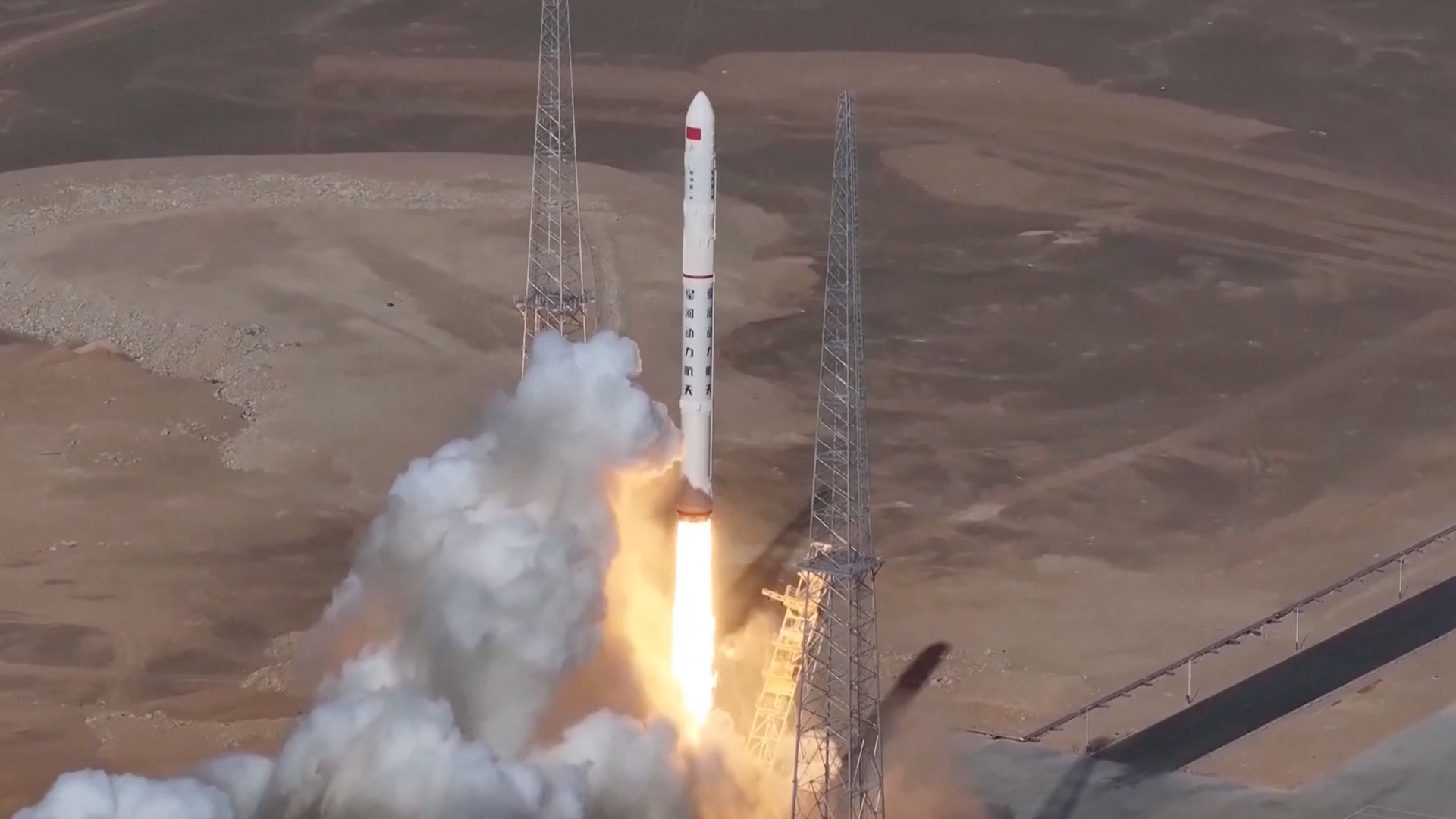 a white rocket launches from a desert pad
