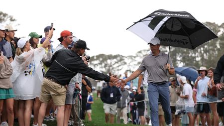 Rory McIlroy low-fives a fan during the final round of the 2025 Players Championship while holding an umbrella