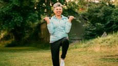 Woman exercises in park on grass, holding dumbbells by her shoulders and standing on one leg