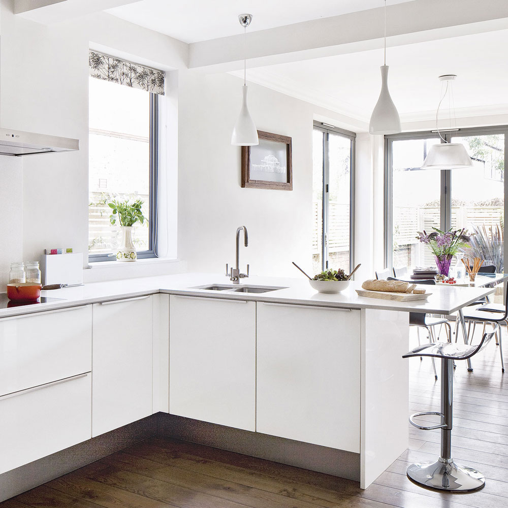 white kitchen with modern kitchen chairs and different lights hanging from the ceiling