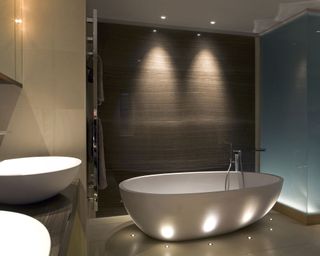 A large white bath in front of a brown with LED uplights and downlights