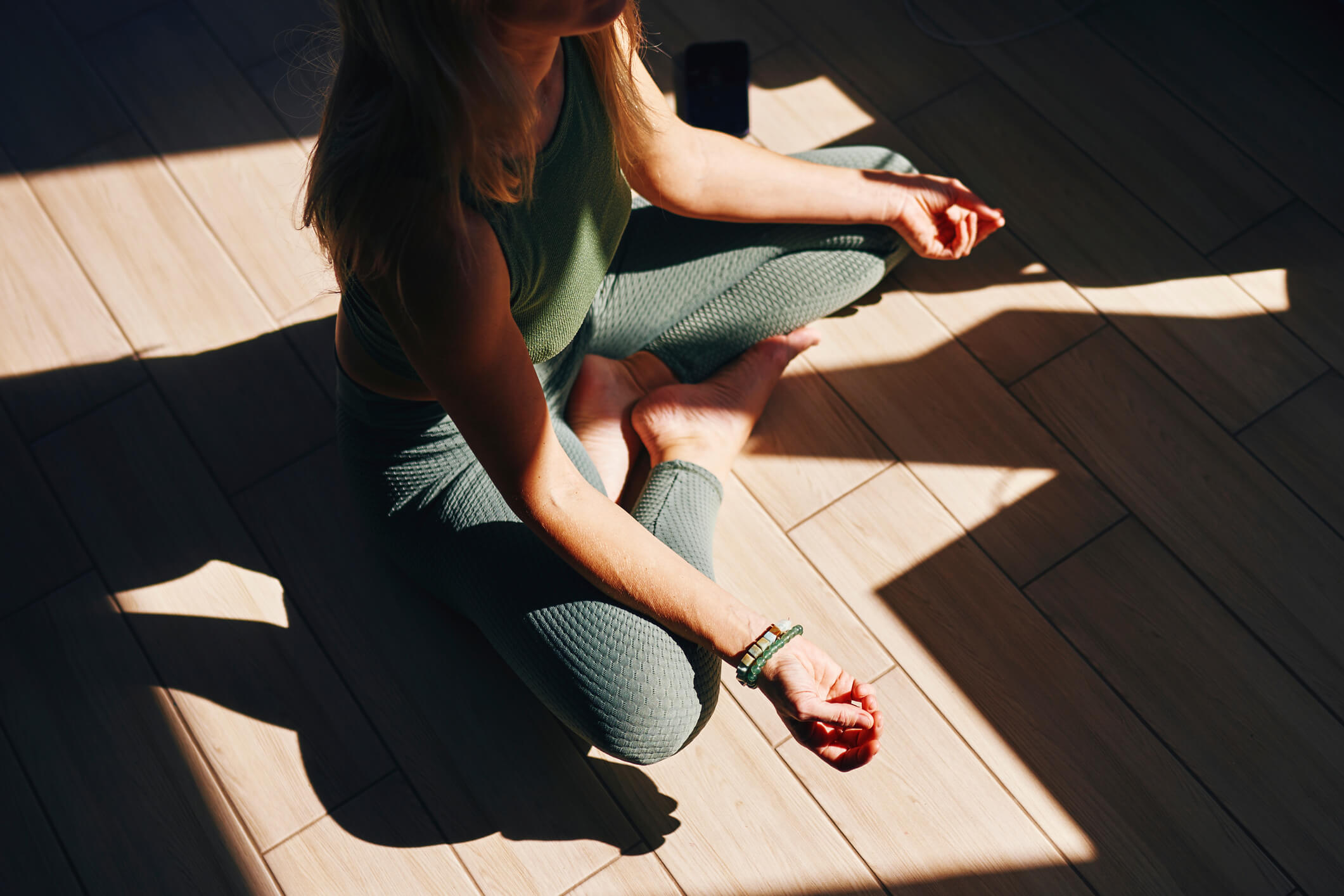 A woman meditating in a space cast in shadows and sunlight.