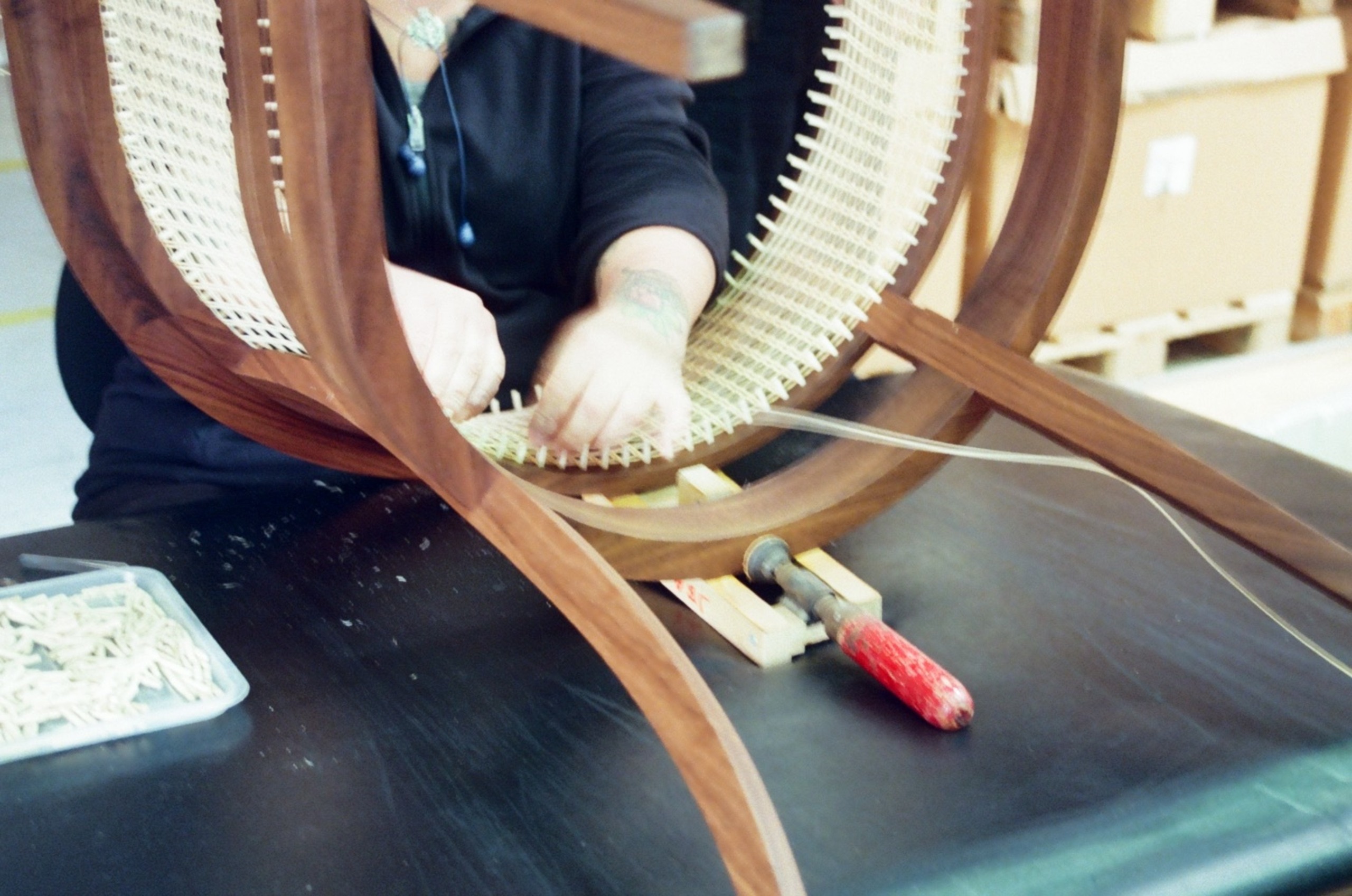 Image of a woman in motion weaving a wooden and rattan chair.