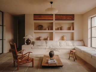 Living room with warm beige limewash walls, built-in shelving and L-shaped seating, wooden furniture and stone floor