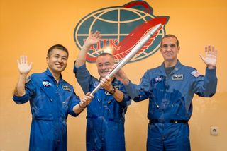 Expedition 38 Flight Engineer Koichi Wakata of the Japan Aerospace Exploration Agency, left, Soyuz Commander Mikhail Tyurin of Roscosmos, and Flight Engineer Rick Mastracchio of NASA, right, smile and wave as they hold an Olympic torch that will be flown with them to the International Space Station, during a press conference held Wed., Nov. 6, at the Cosmonaut hotel in Baikonur, Kazakhstan.