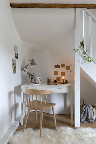 a scandi home office under the stairs, with a white desk and wooden chair, and a fluffy white rug on the floor