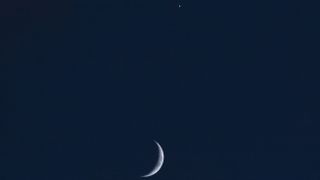 a thin crescent moon beside a pale yellow orb