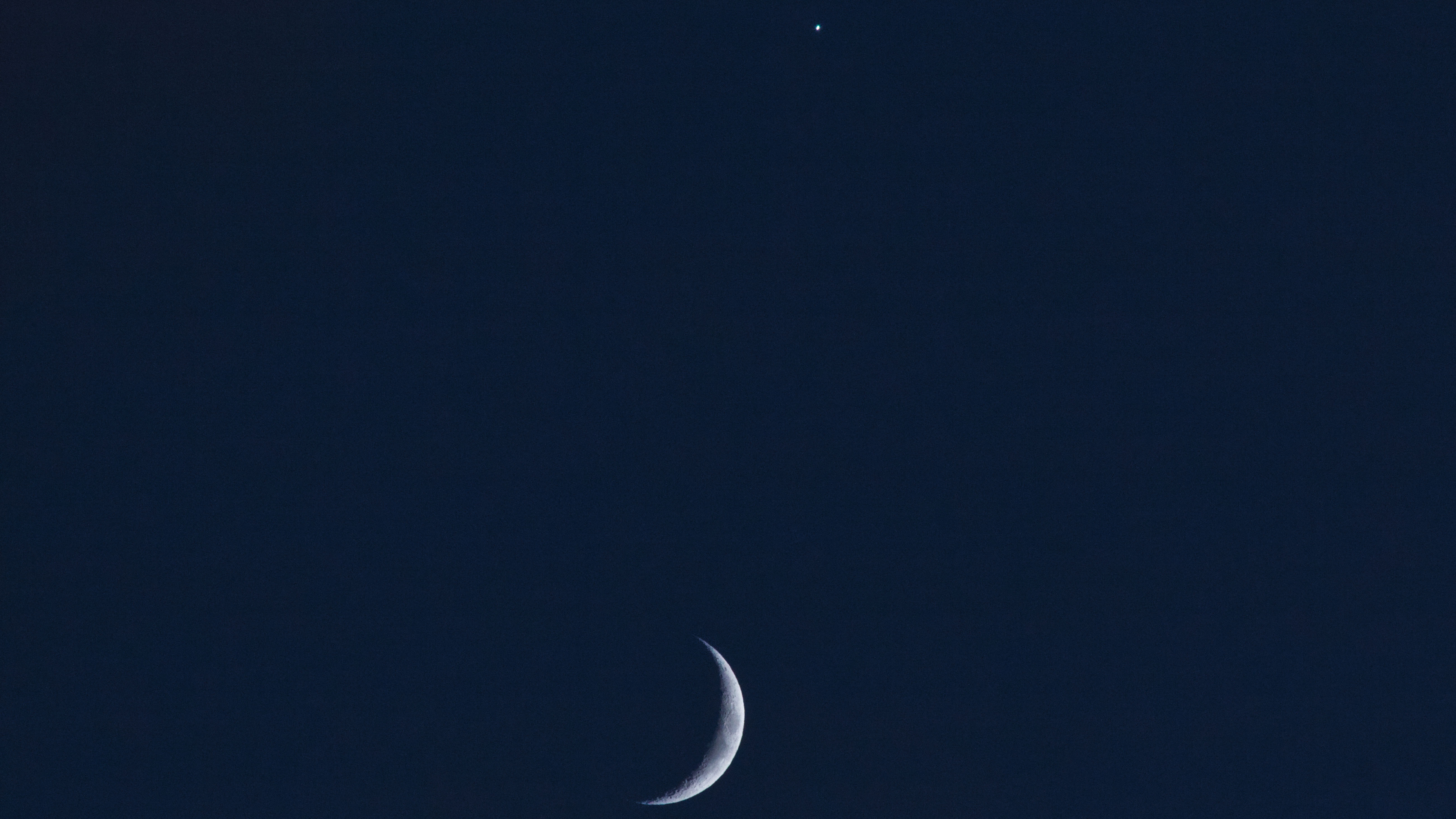 a thin crescent moon beside a pale yellow orb