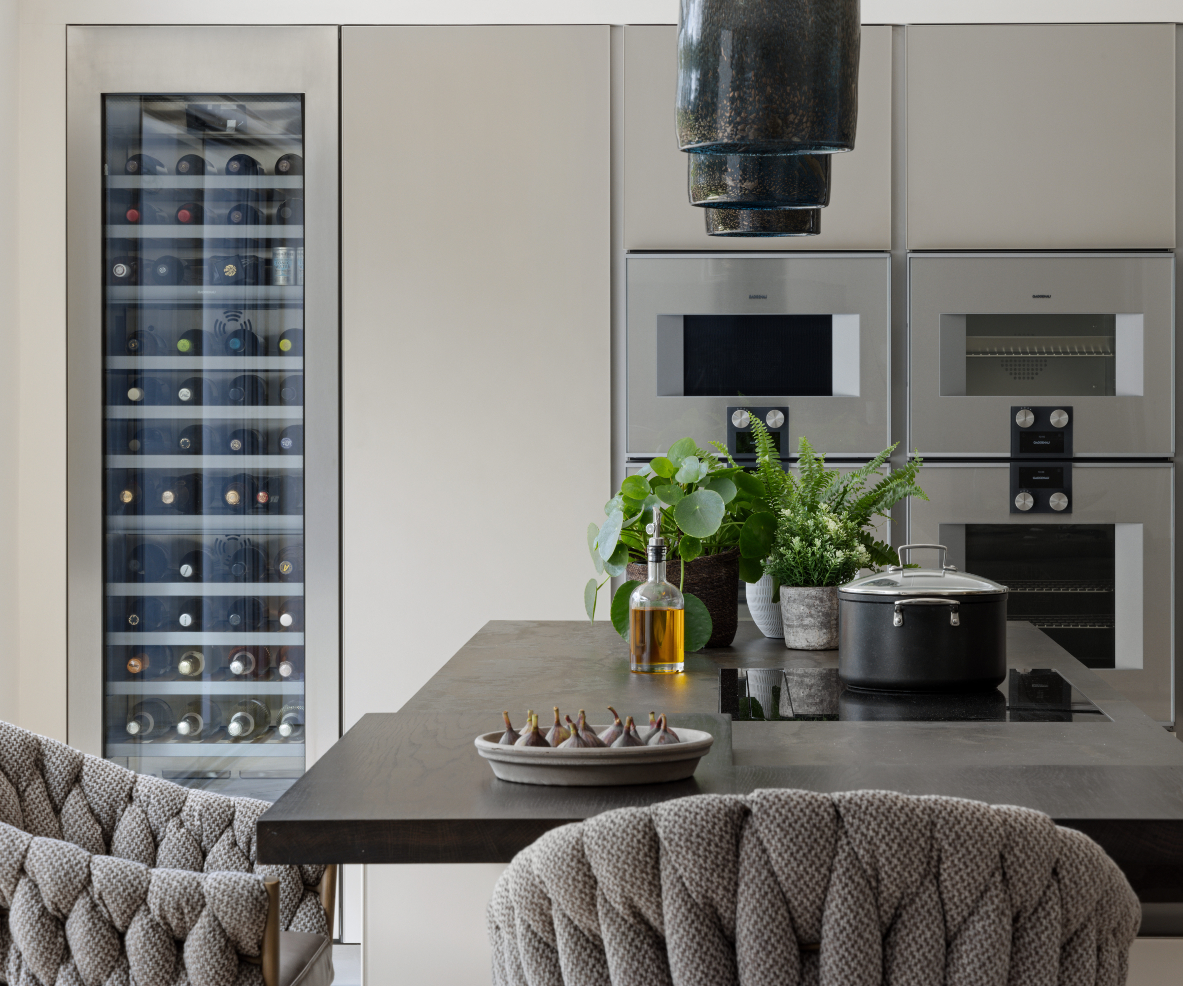 kitchen island with seating, inset hob with large wine fridge and integrated ovens in the cabinets behind the island