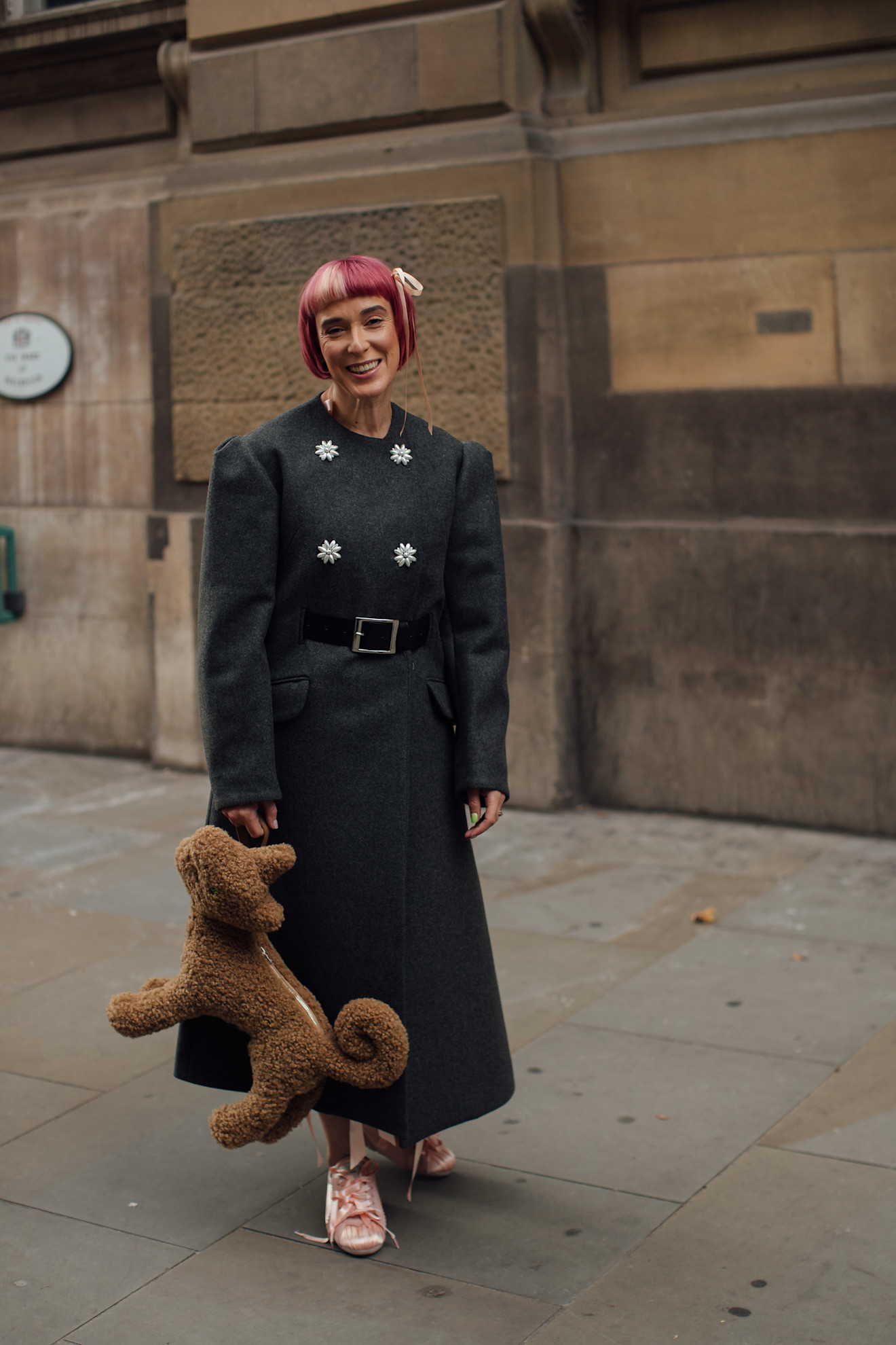 girl standing in a gray coat holding a dog-shaped purse with pink hair