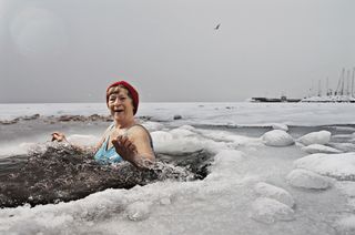 A woman bathes in a hole in the ice on a frozen sea.