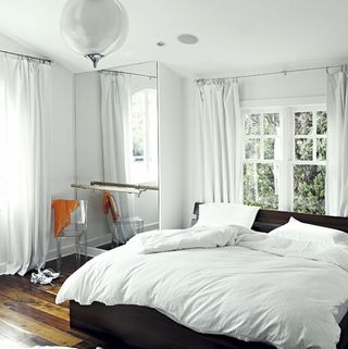 bedroom with white wall bed with white cushion window and wooden flooring