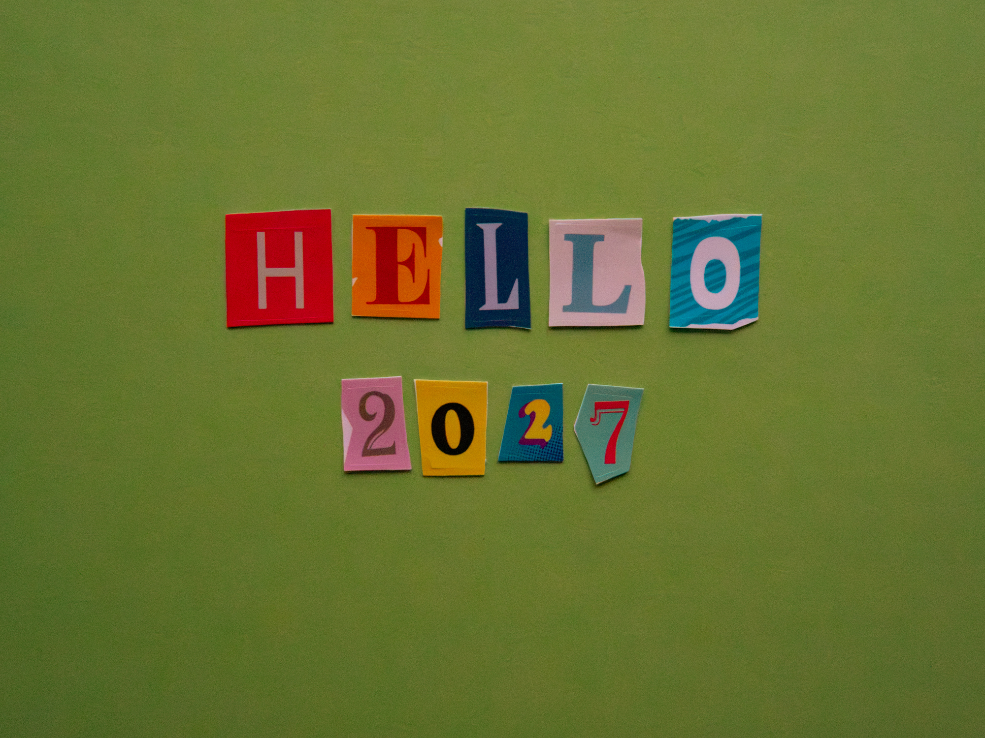 Creative &amp;ldquo;HELLO 2027&amp;rdquo; message made with colorful magazine-style cutout letters and numbers on a green background.