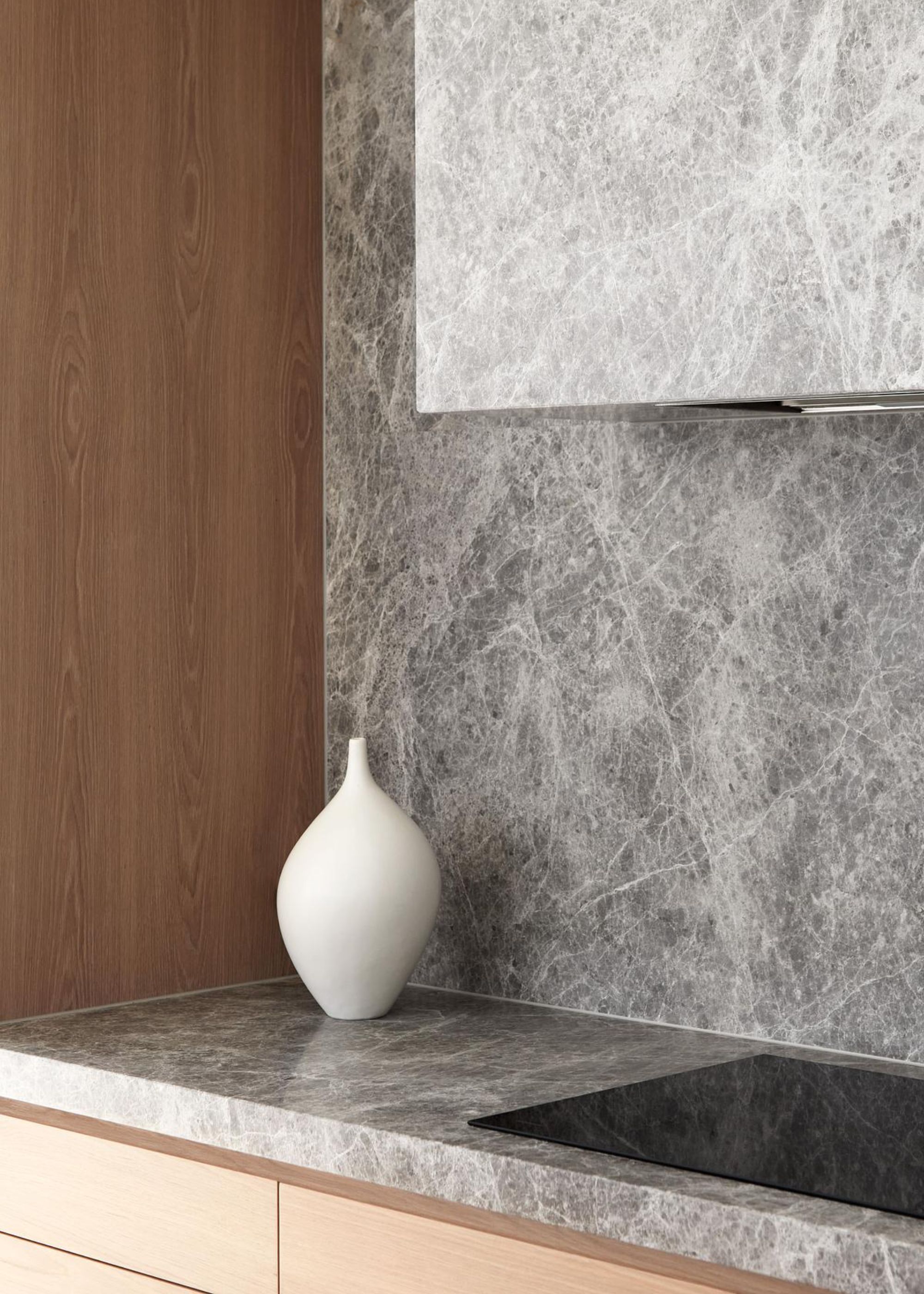 The corner of a kitchen countertop in grey with a white vase next to it. There is also a view of the corner of the stove top.