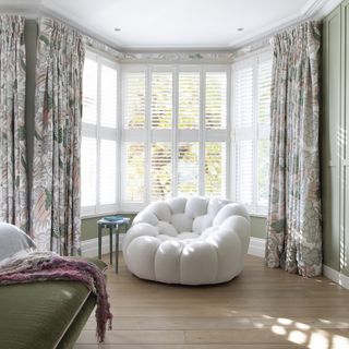 living room with white shuttered windows, wooden flooring, white armchair and patterned curtains