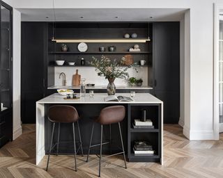 A black galley kitchen with white walls and countertops and statement lighting over a breakfast bar.