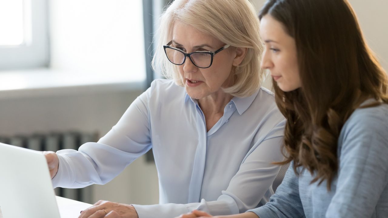 An older woman and a younger women look at a laptop together at a table.