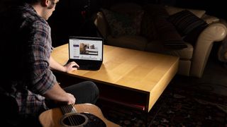 Man views TrueFire on a laptop whilst holding an acoustic guitar