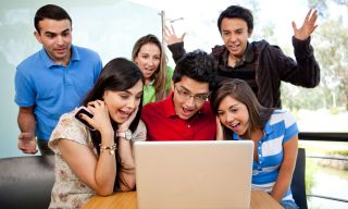 Teens gather around a laptop computer with delighted expressions. 