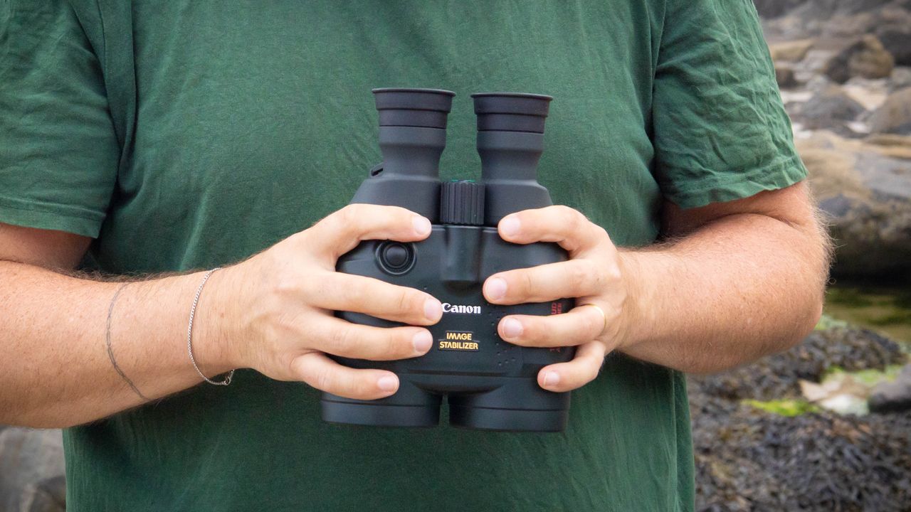 A male holding the Canon 18x50 IS binoculars close to their chest showing the image stabilization label and Canon logo.
