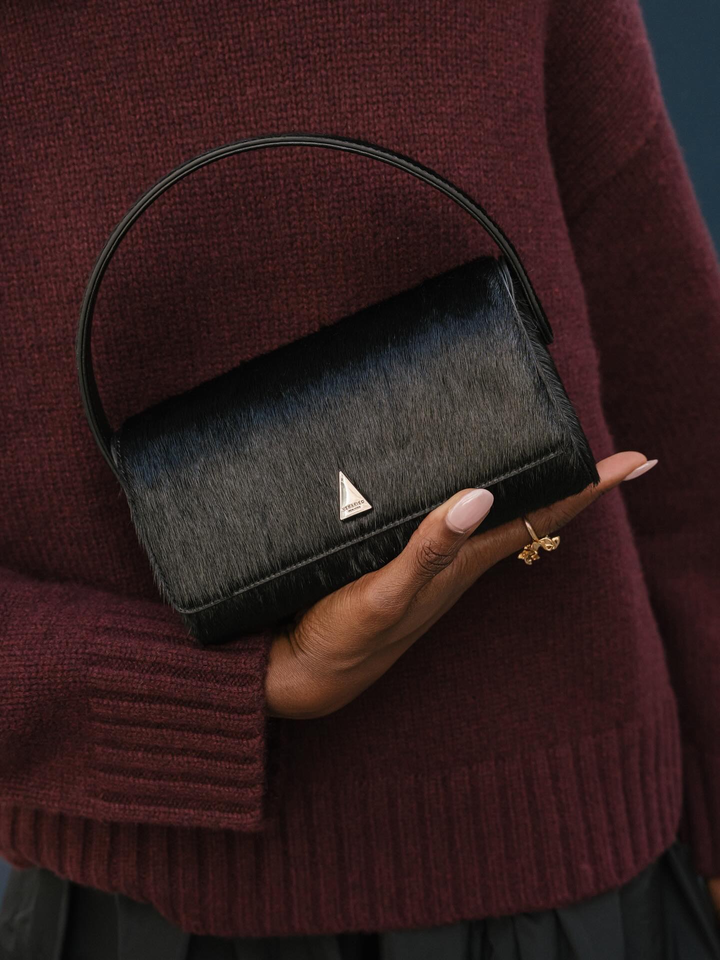 A photo of @emmanuellek_ in a burgundy jumper holding a black mini bag with sheer pink nails
