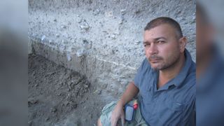 University of Ankara archaeologist Vasif Şahoğlu, seen here beside layers of ash from the Thera eruption, led excavations at the site for 10 years.