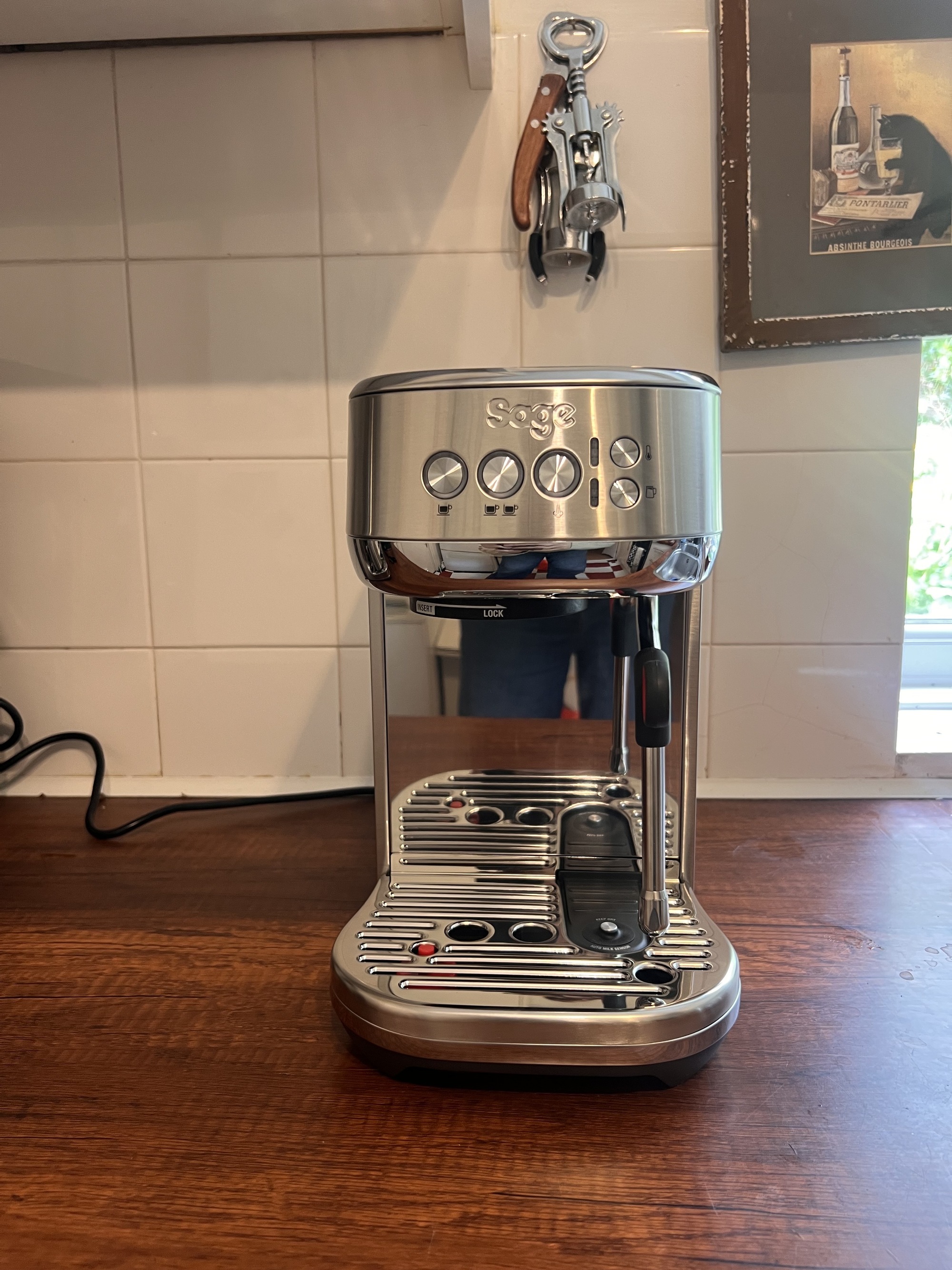 Image of a silver Sage Bambino Plus on a wooden countertop in front of a white tile backsplash.