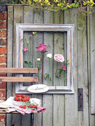 Pink roses and white flowers in a wooden frame hung on a garden gate.
