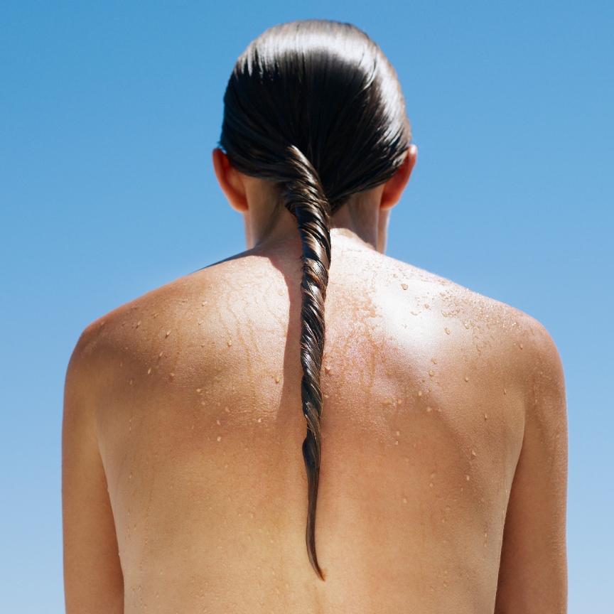 a woman's bare back in the sun with wet hair in a twist