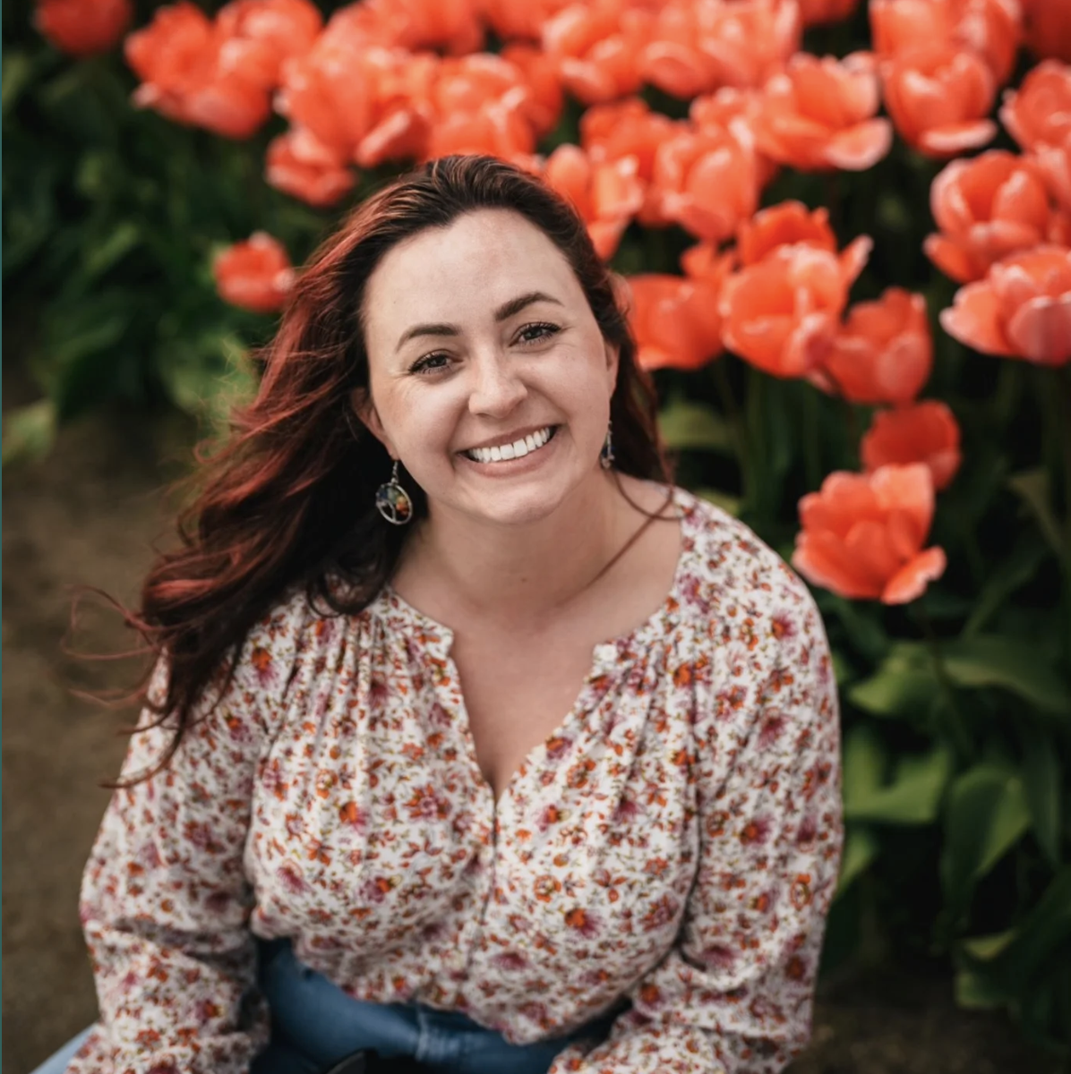 woman with brown hair wearing floral top with red flowers in the background