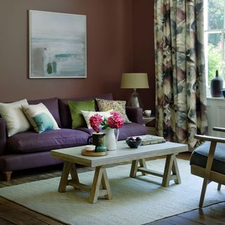 A purple living room with mauve walls, a wooden coffee table and floral curtains