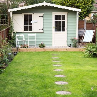 green garden shed with stepping stone pathway in grass