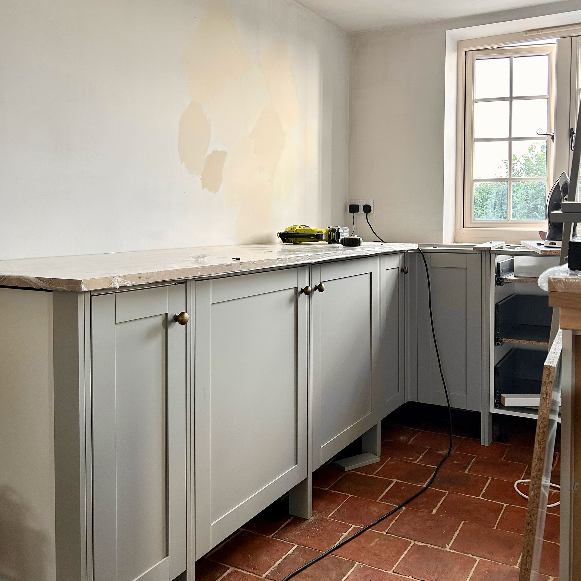 Cabinets being fitted into kitchen mis-renovation, with paint swatches on wall above
