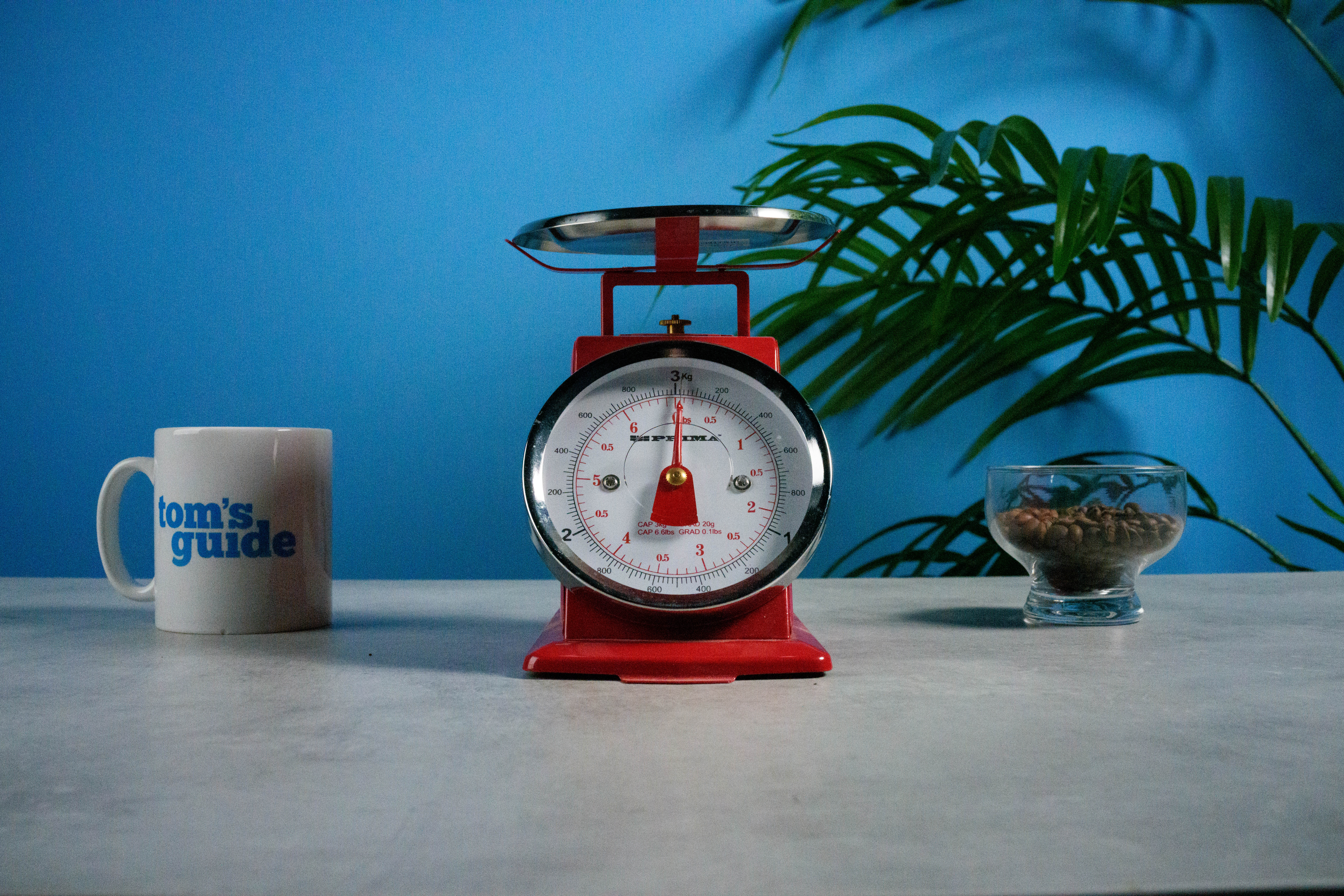 A photo of a set of red scales next to a Tom's Guide mug and some coffee beans, with a blue wall in the background