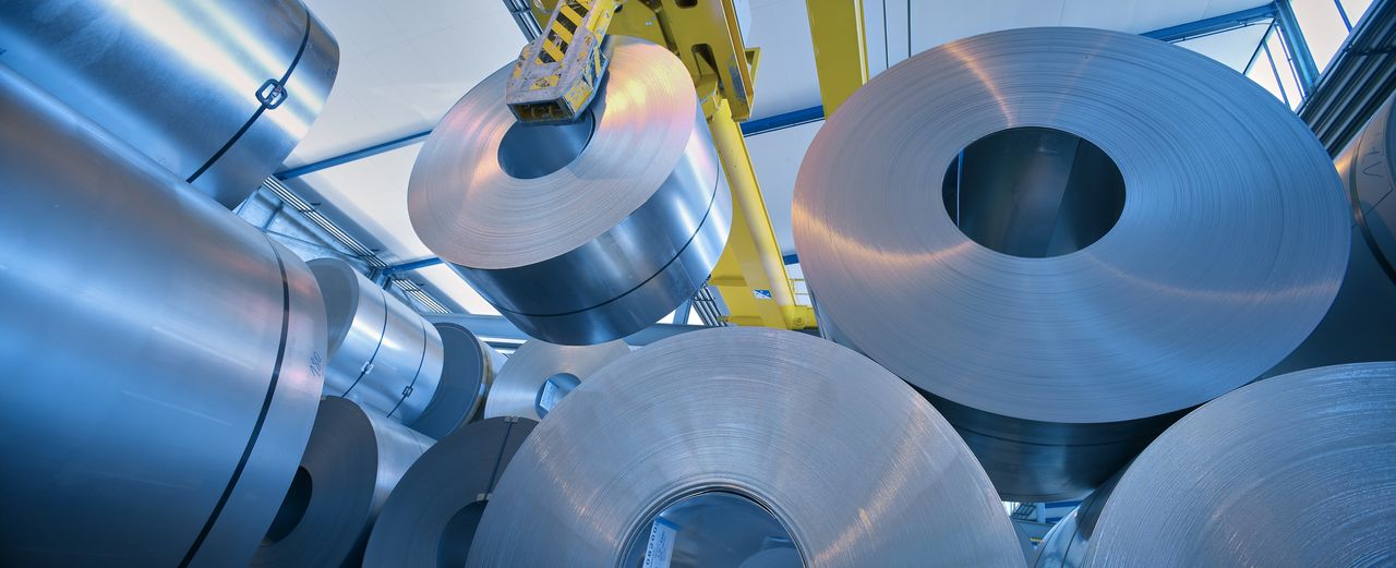 rolls of steel being moved by a large yellow machine