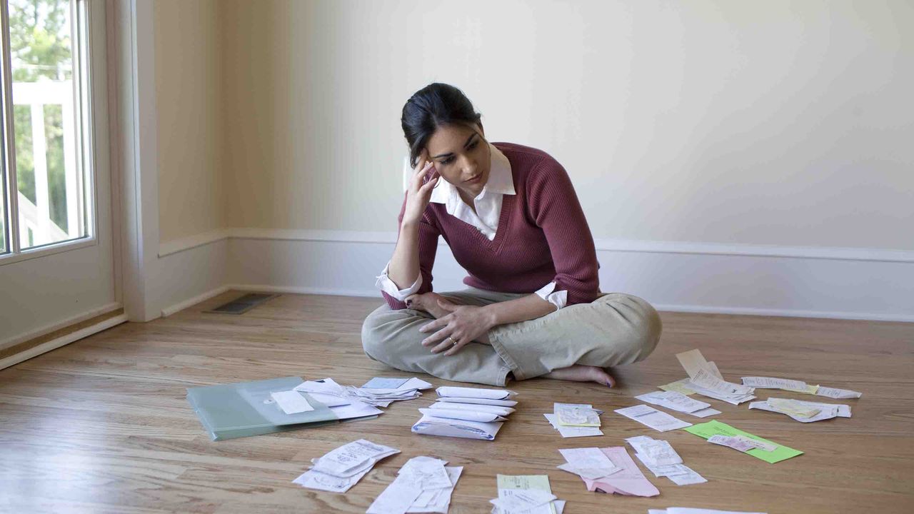 Photo of a woman sitting on the floor surrounded by bills