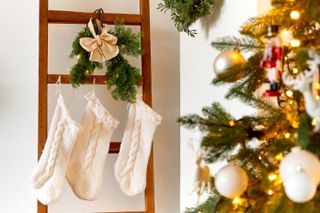 Festive Christmas decorations of a light room with a Christmas tree and knitted socks hanging on a ladder.