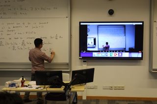 A teach at a whiteboard in a classroom at Shanghai NYU powered by Dante audio network for remote learning.