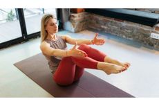 Woman holding boat pose, balanced on her sit bones with her legs raised and arms extended at shoulder height
