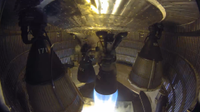 One of six rocket engines in an enclosed aft rocket section fires into a test stand.