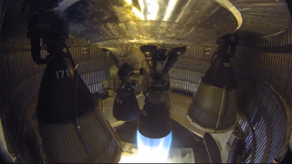 One of six rocket engines in an enclosed aft rocket section fires into a test stand.