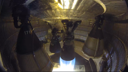 One of six rocket engines in an enclosed aft rocket section fires into a test stand.