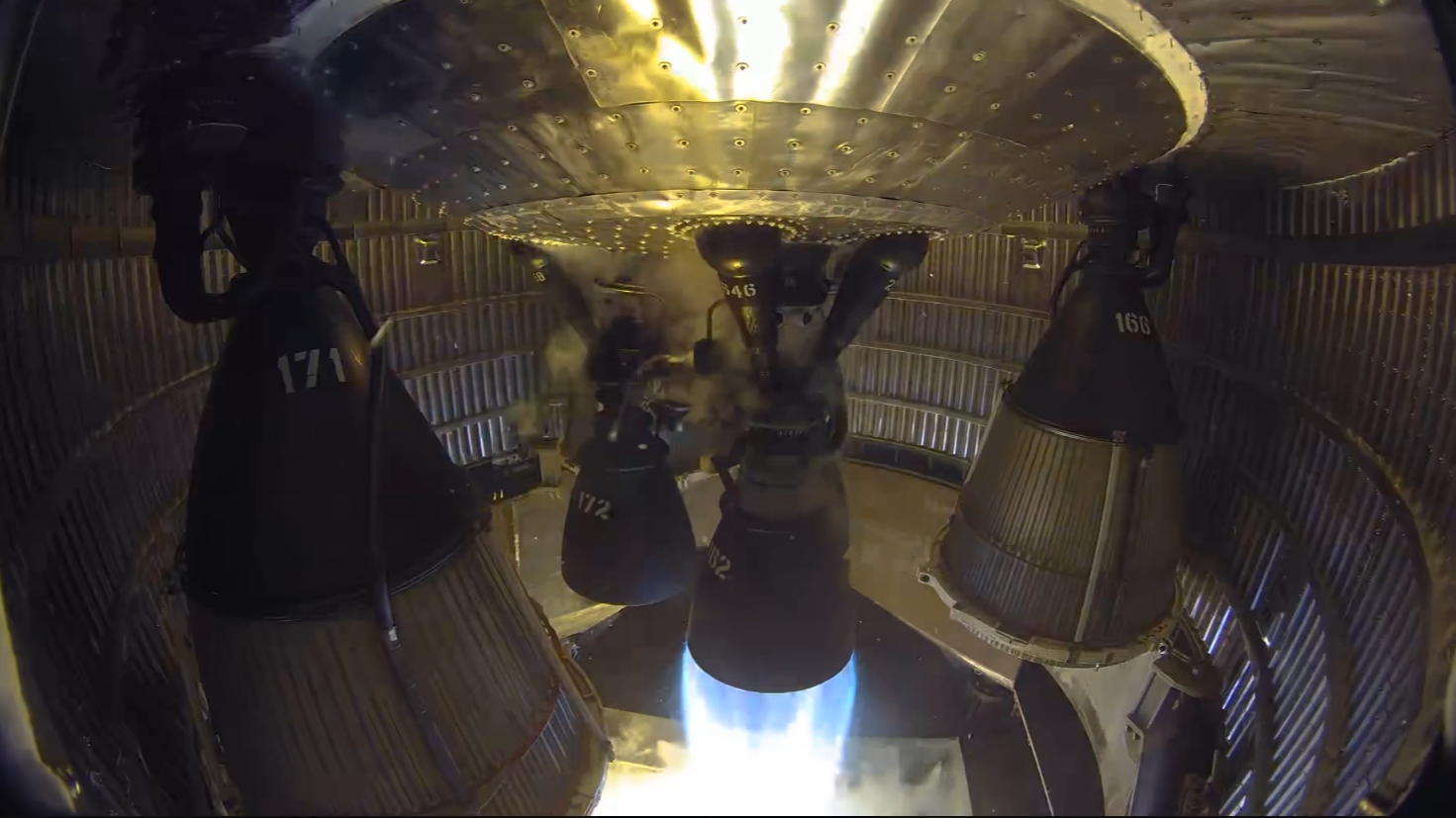 One of six rocket engines in an enclosed aft rocket section fires into a test stand.