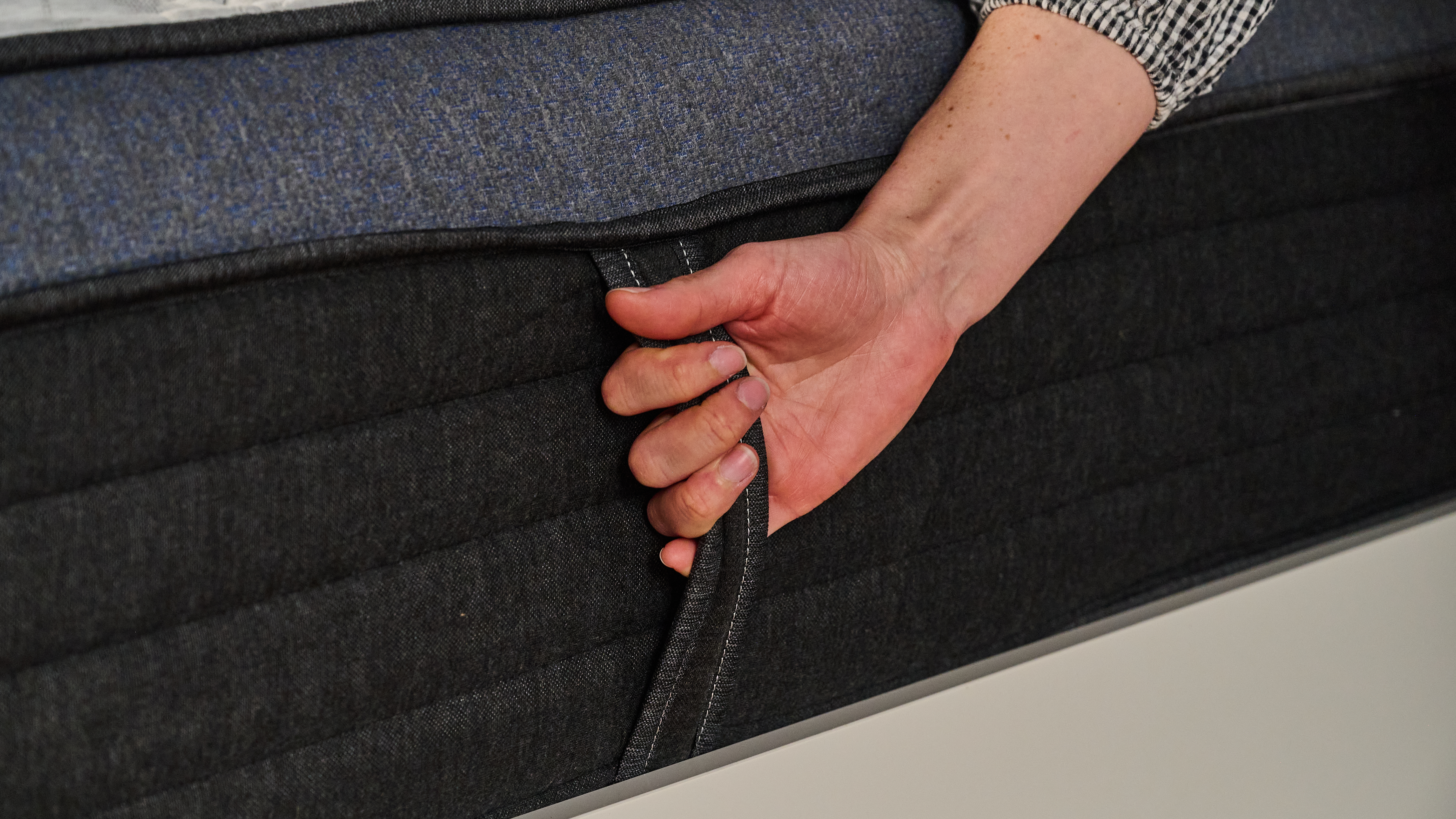 The image shows a close up of a hand grasping the side handle on the Helix Midnight Luxe mattress