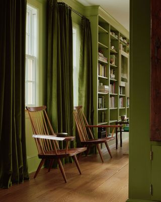 a green painted room with green curtains. two classic wooden chair sit under each window