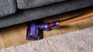 the dyson gen5detect cordless stick vacuum in prussian blue and copper, showing its cleaning head and attachment tools