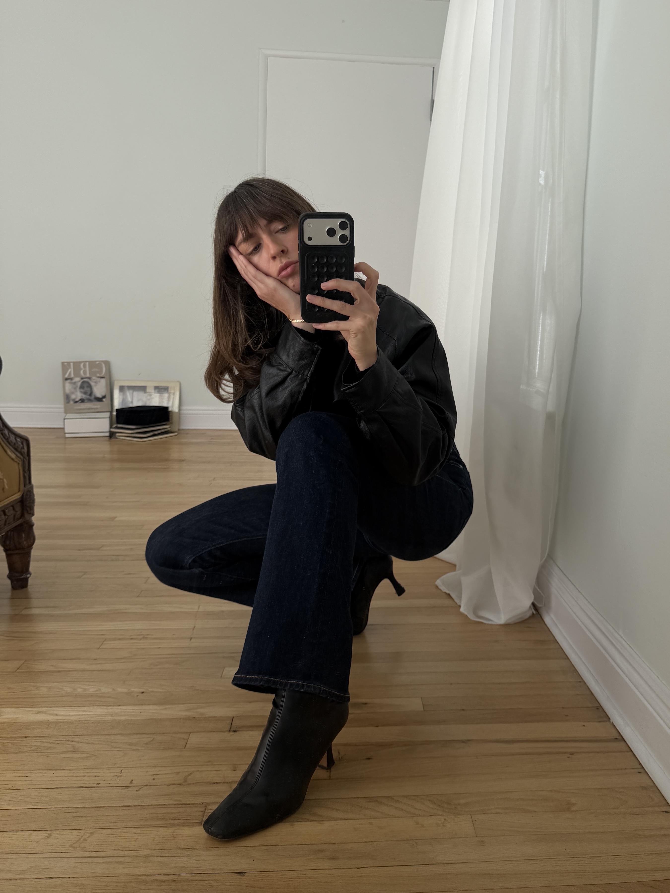Kathryn Zahorak posing in mirror wearing leather jacket, dark wash jeans, and black boots