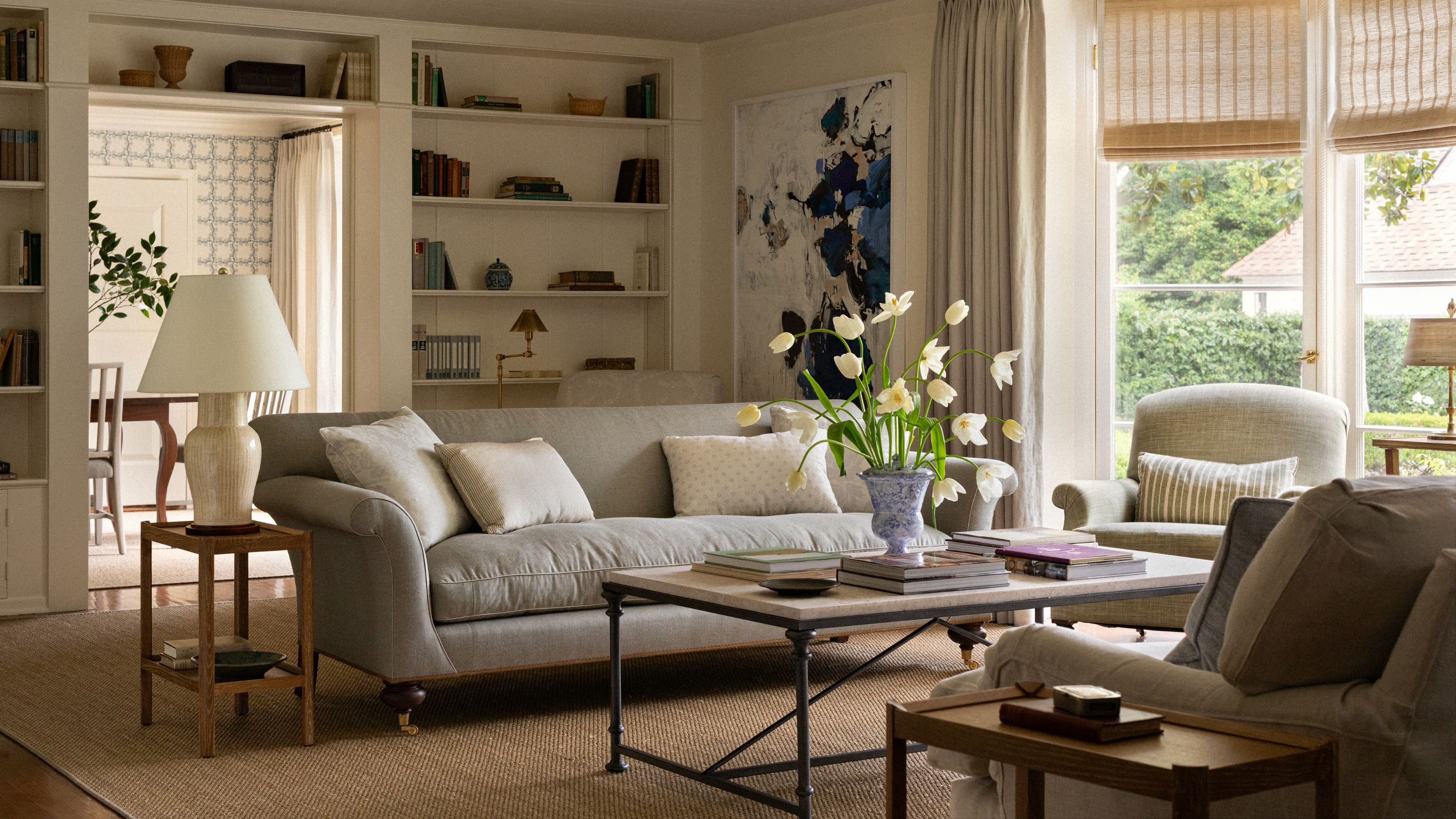 a warm neutral living room with a bookcase built around the doorway into the dining room